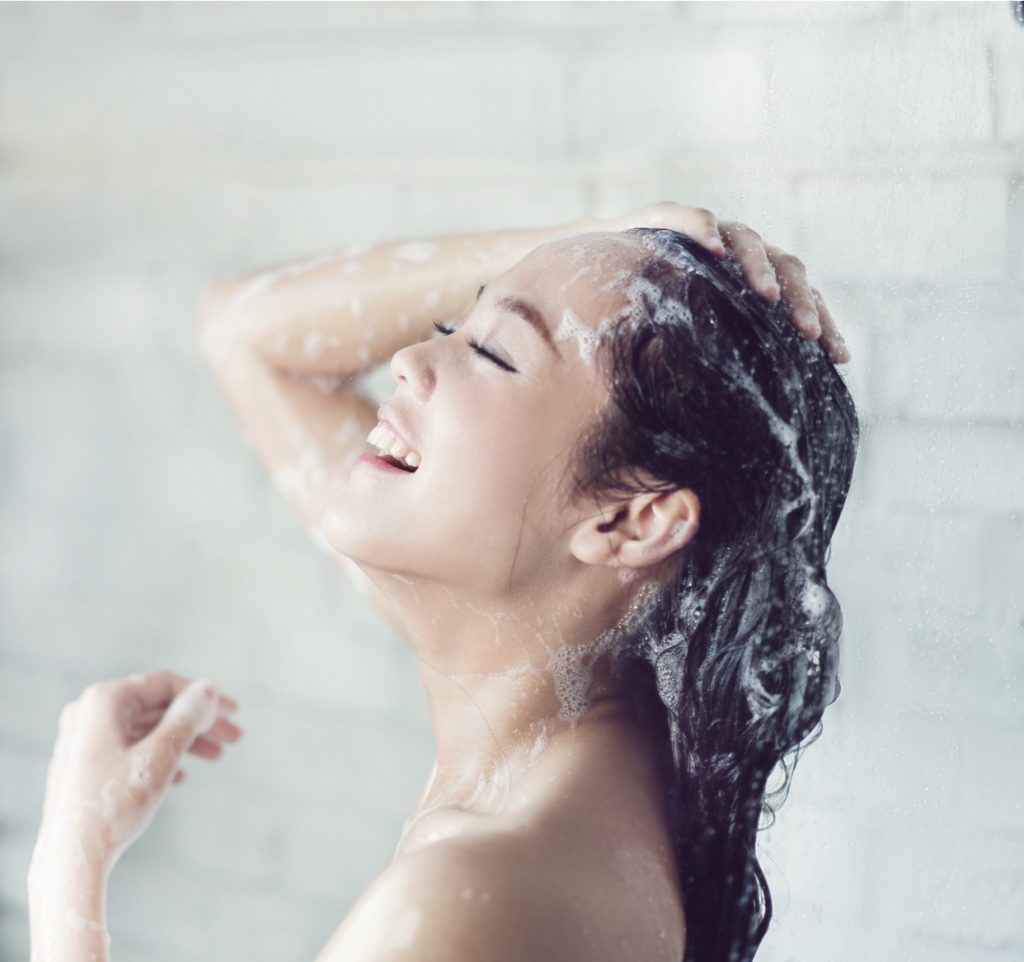 femme se lavant les cheveux sous la douche avec un shampoing bio
